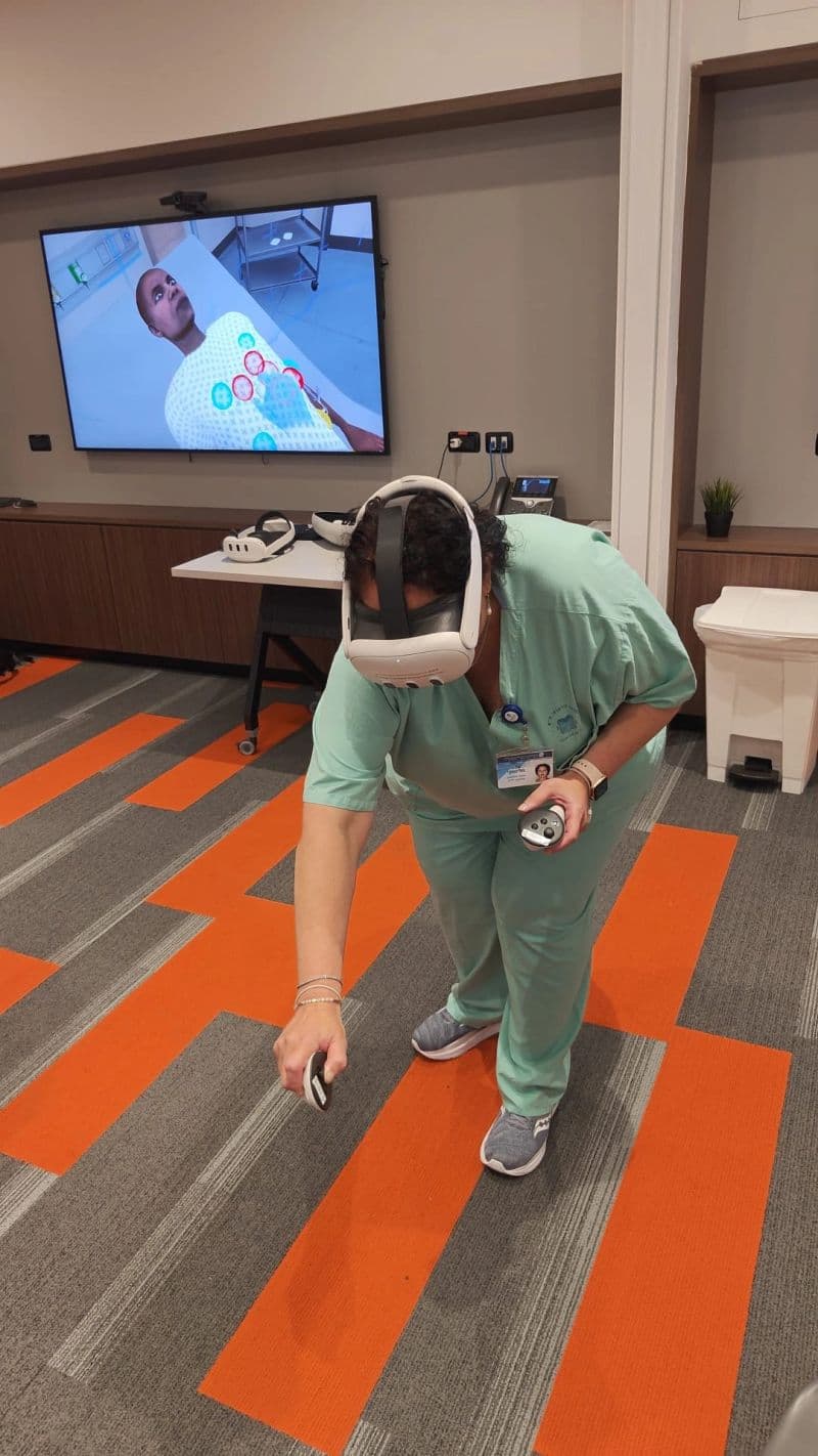 A nurse in scrubs and a VR headset reaching toward a virtual patient during an InvolveXR scenario, the simulation shown on the screen behind