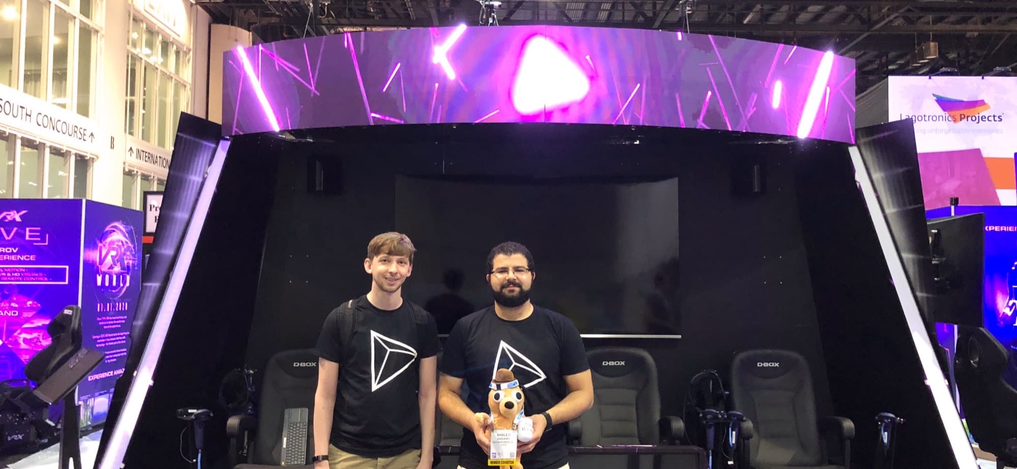 Khaled and a teammate standing in front of the Vusr Stage booth's row of D-BOX motion chairs under a curved LED display
